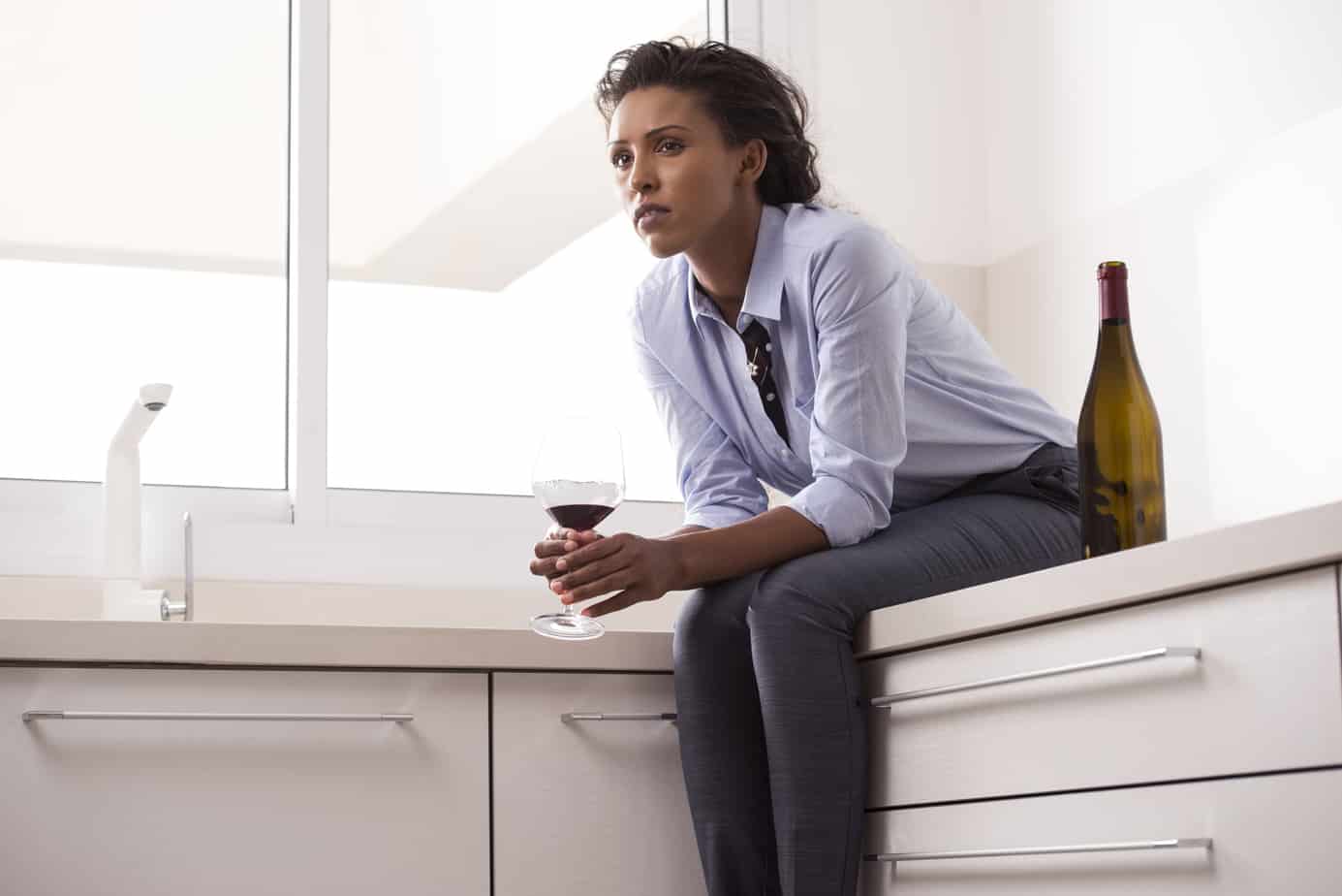 stressed woman hiding in bathroom with bottle of wine and full glass
