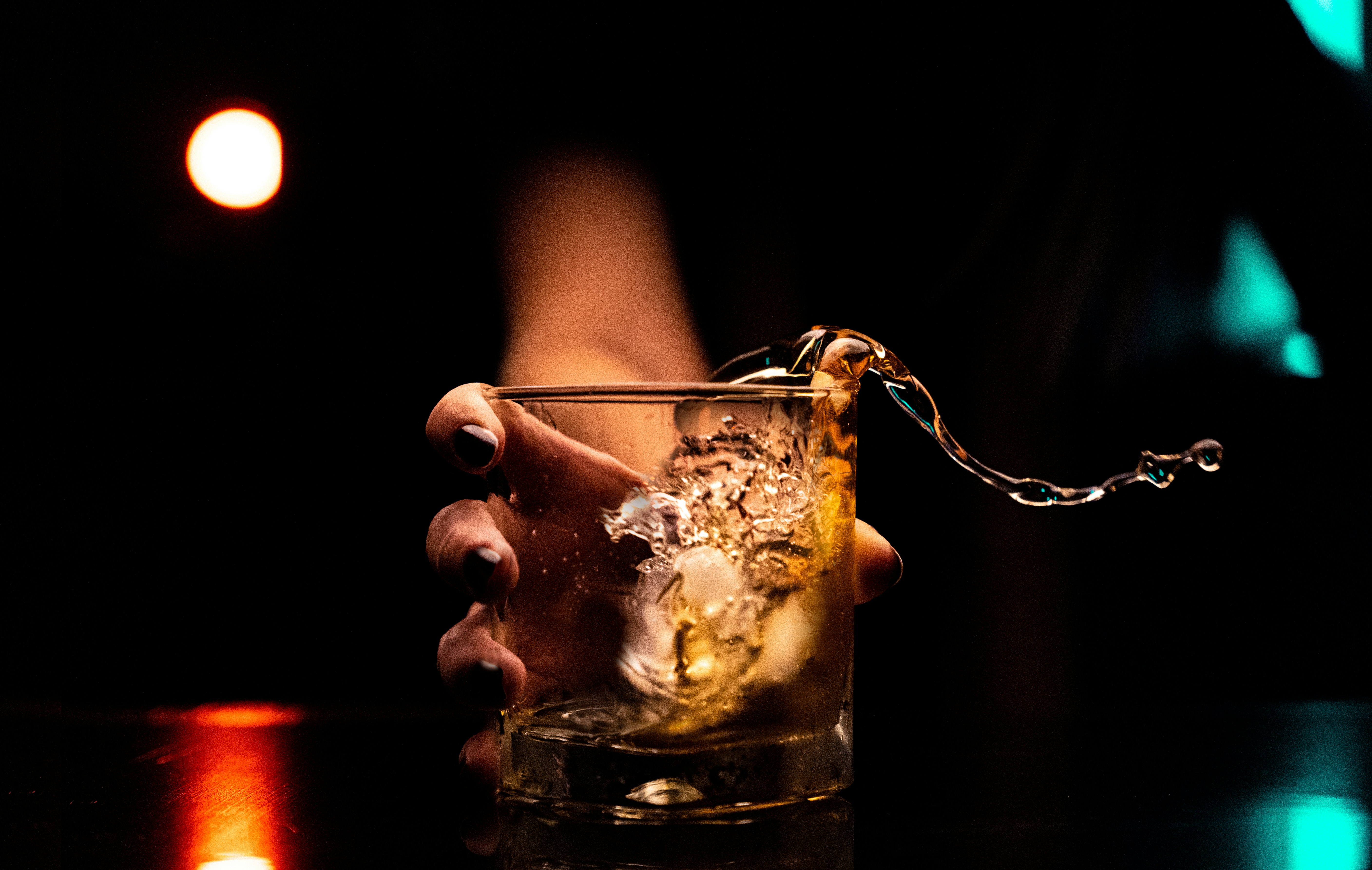 Woman's hand grips an alcoholic drink in which a chain dangles from