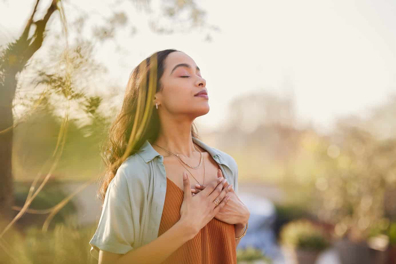 woman practicing gratitude outdoors in nature, holding hands to chest