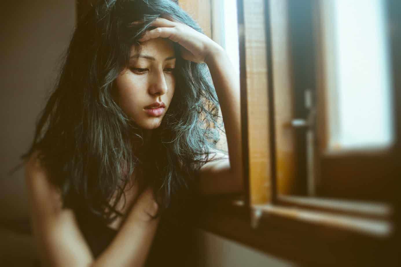 Young woman experiencing drug withdrawal sits in front of mirror and sadly looks at floor