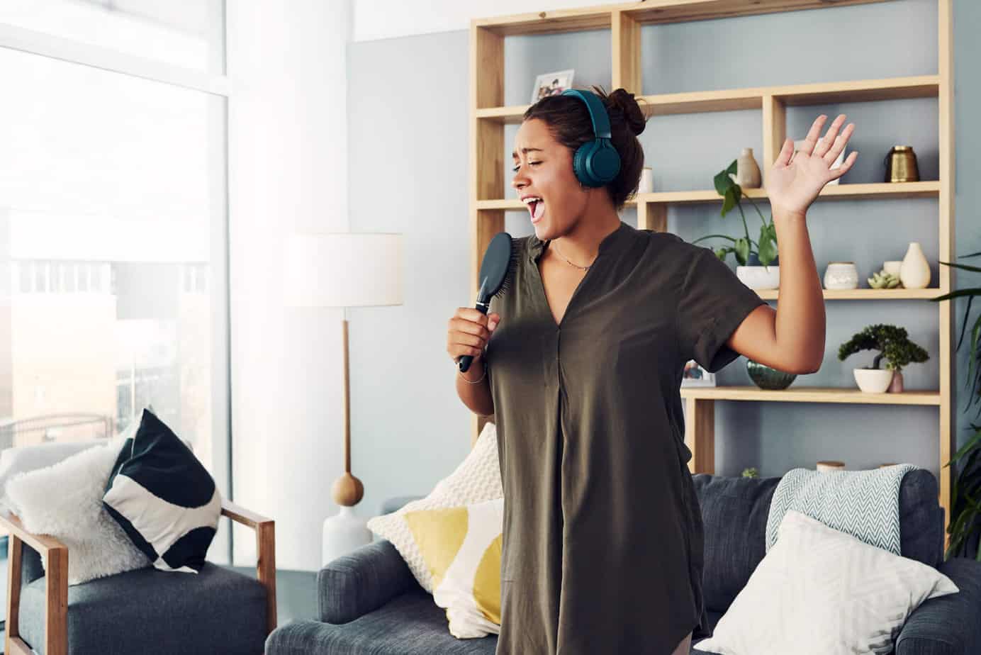 happy woman singing in living room wearing headphones holding microphone