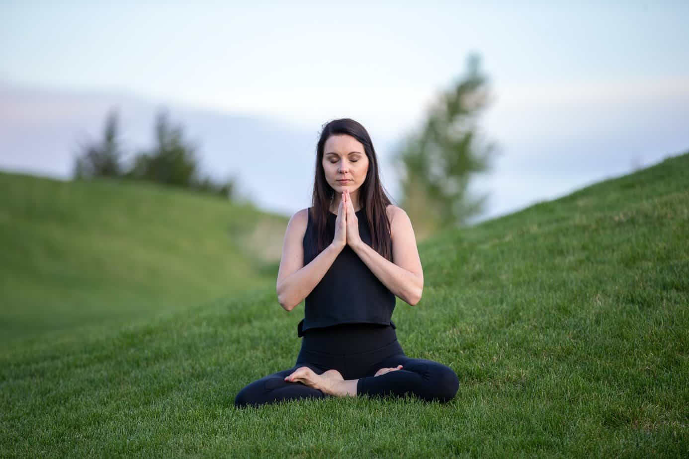 woman sits on grass in yoga pose meditating in recovery