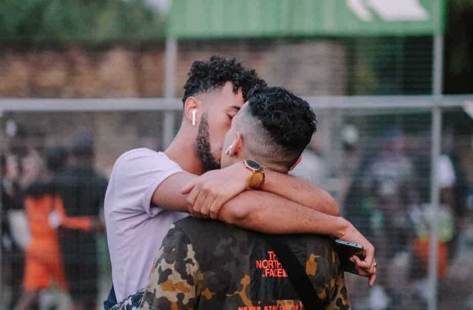 Two gay men embrace and kiss each other outdoors