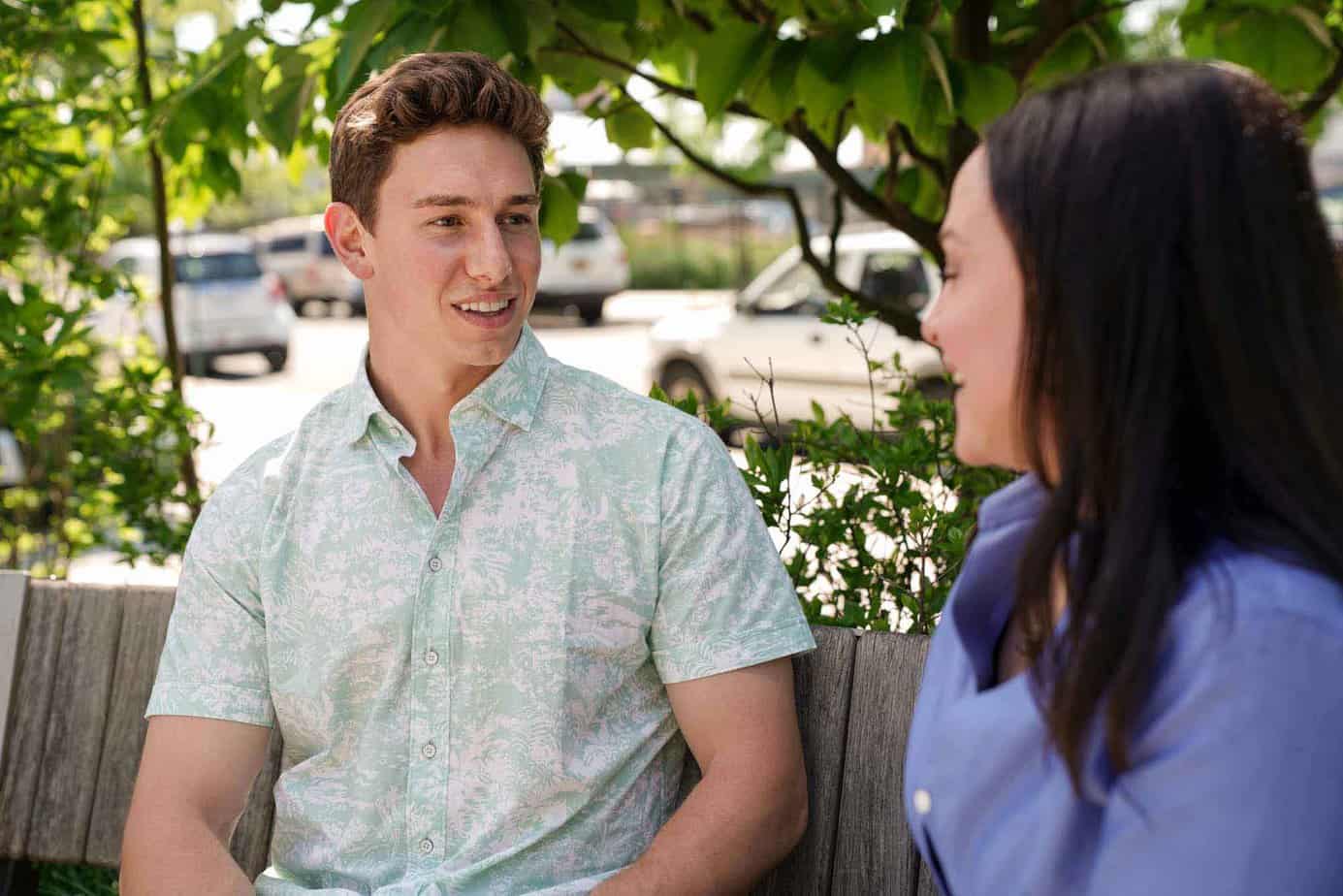 Young male sitting with his recovery coach on a bench near a tree, discussing addiction and sober living.