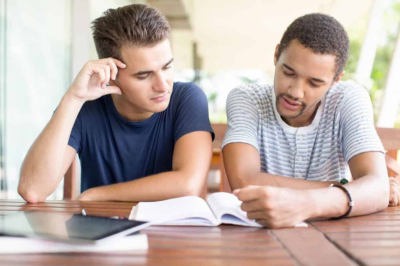 Two male students reading a book together