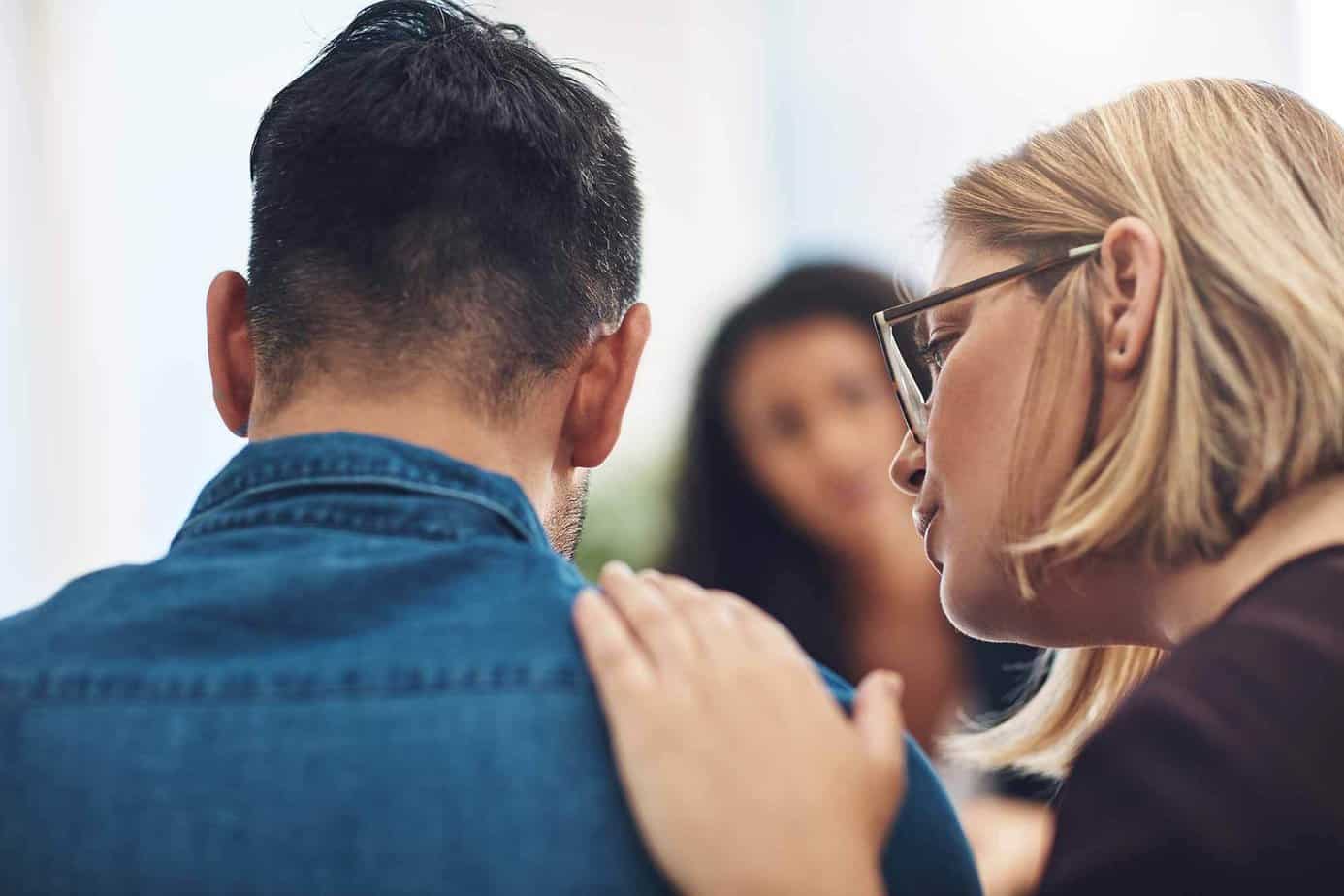 A woman with glasses comforting a man in a denim shirt who is starting addiction treatment at Mountainside
