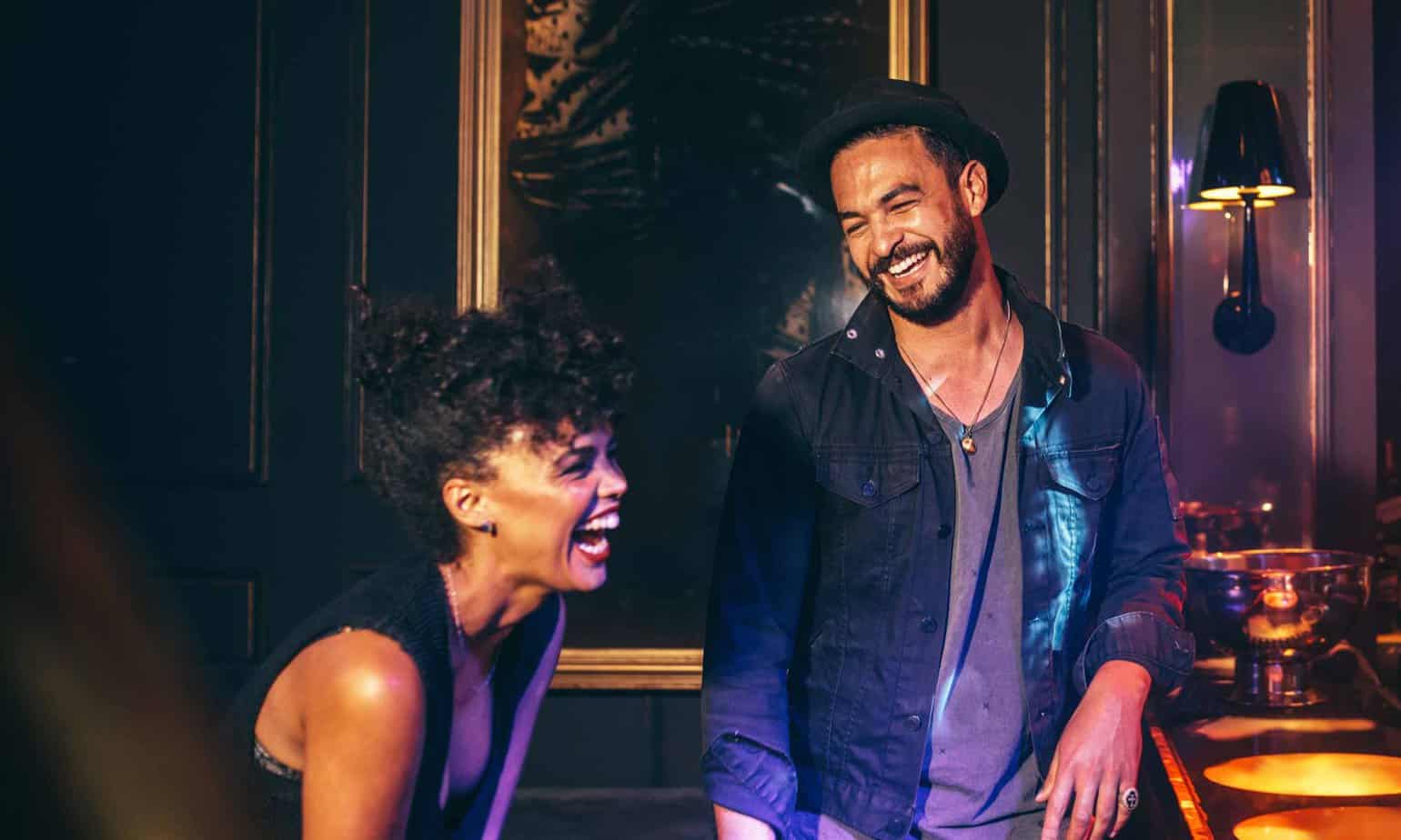 Man and woman laughing and smiling behind painting in a bar