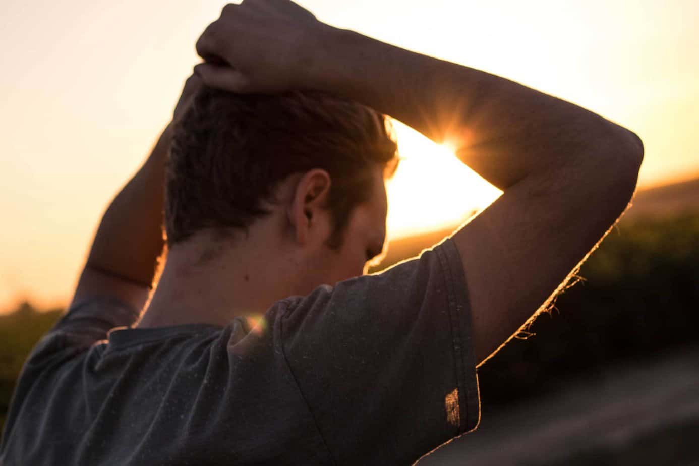 man in addiction recovery holding his hair in hands and struggling with grief outside with sunset