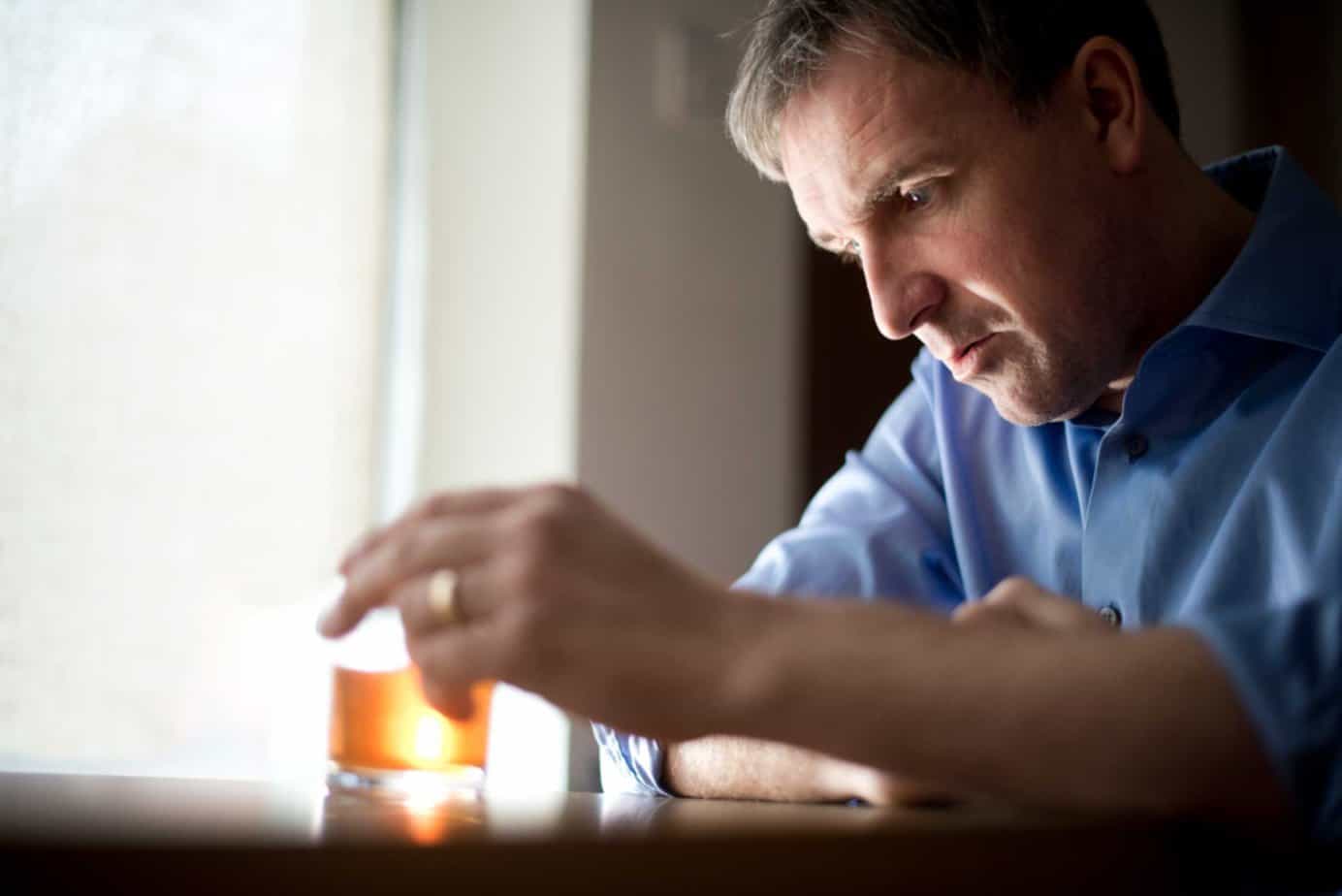 A man sits at a table with a drink and a distressed face.