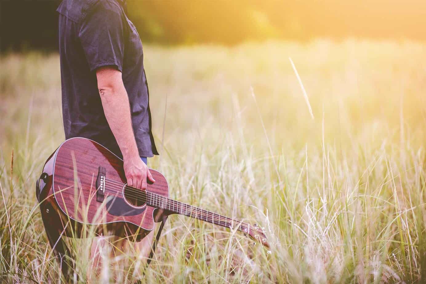 man in field holding a guitar