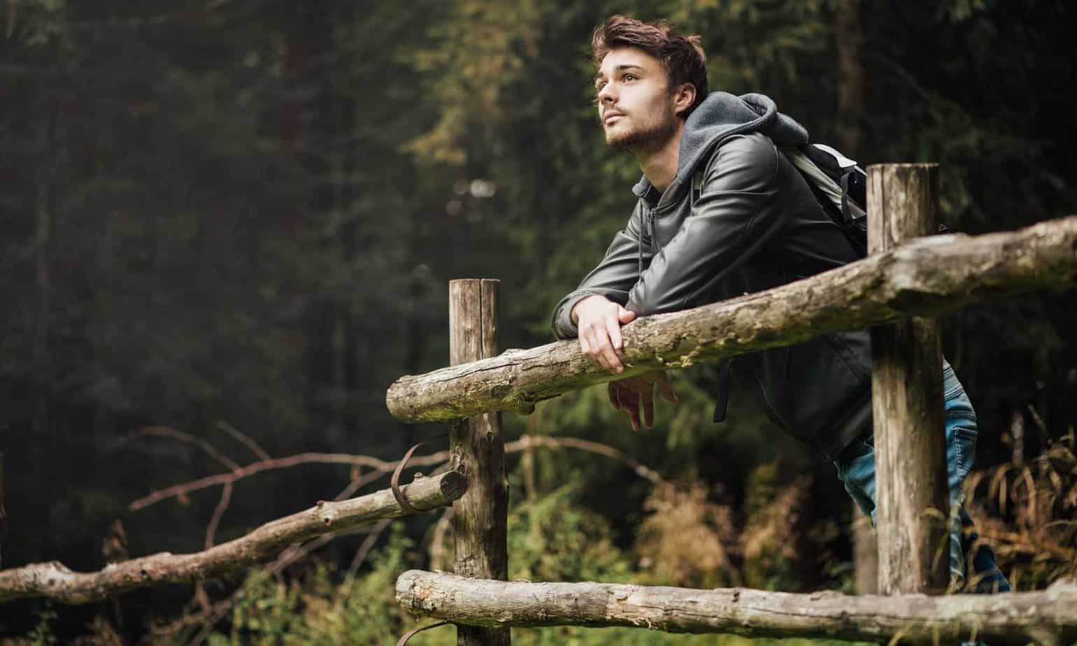 man on wooden fence in woods looking out to the distance