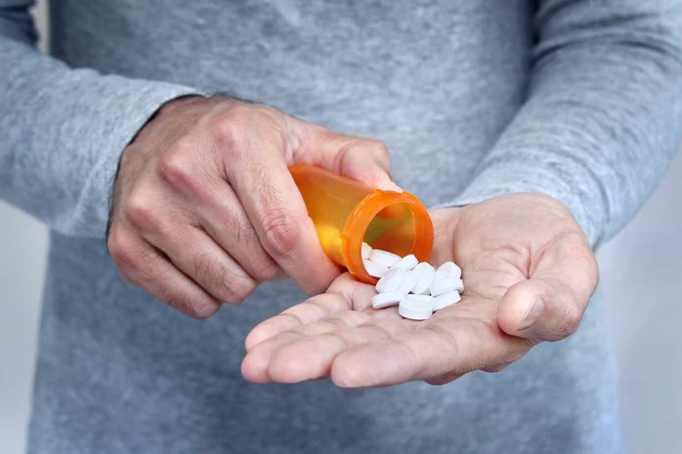 Man managing chronic pain in recovery empties opioid pills from a bottle into his hands