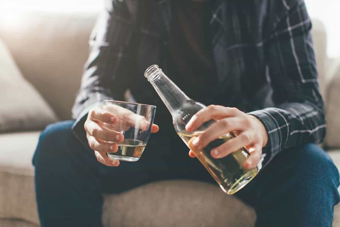 man seated on couch pouring liquor from bottle into glass