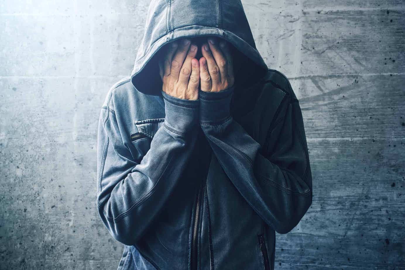 person in a hoodie struggling with heroin addiction covers their face with their hands