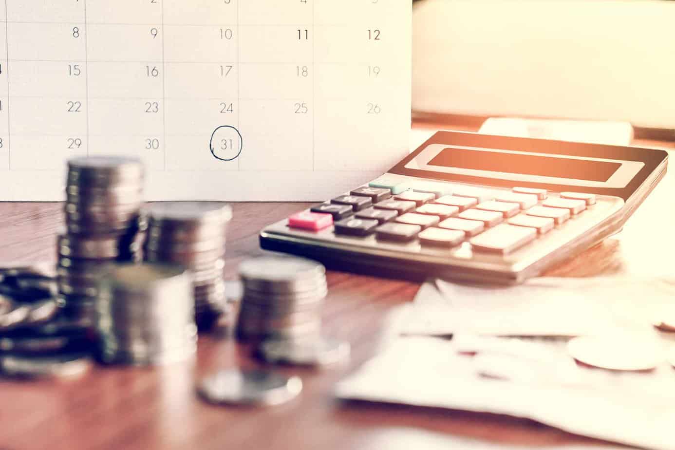 various coins and calculator placed on desk in front of calendar for financing