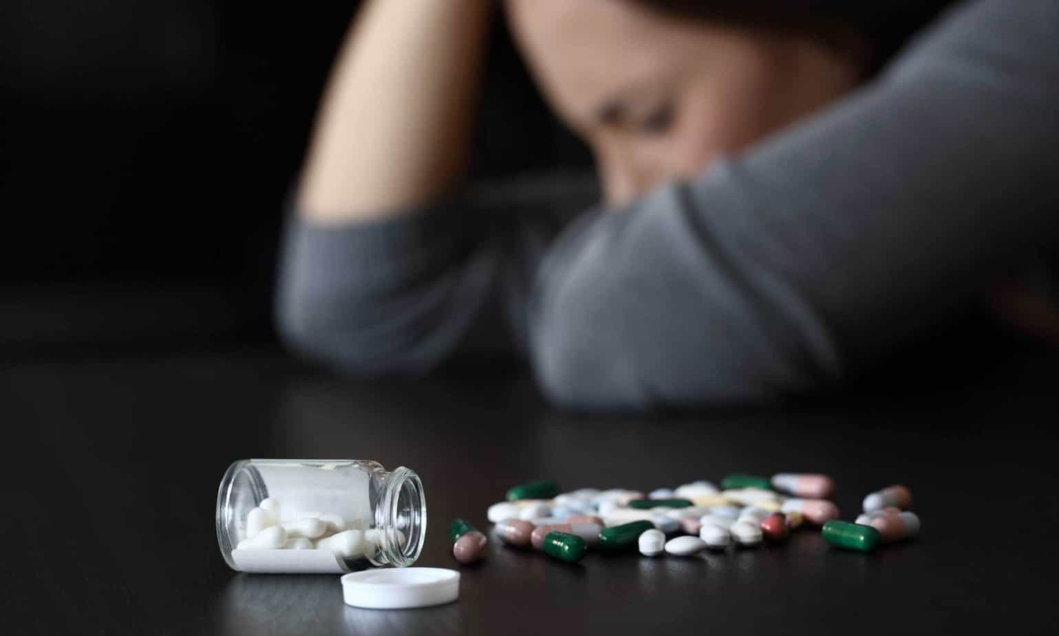 woman struggling with addiction with pills spilled on table