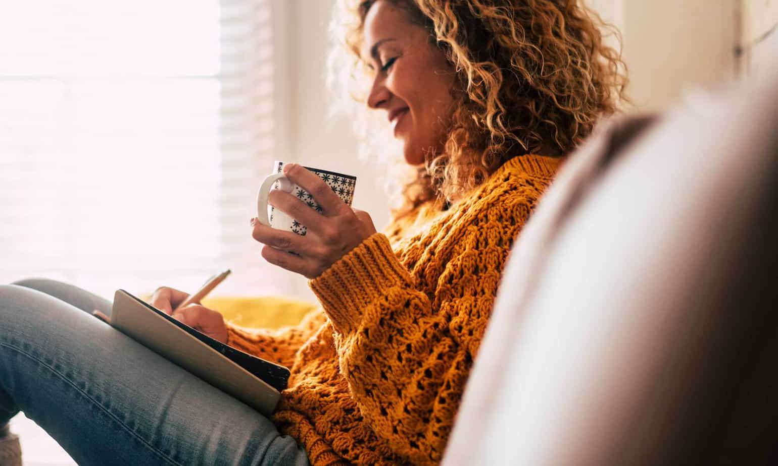 smiling woman drinking tea and writing notes in journal