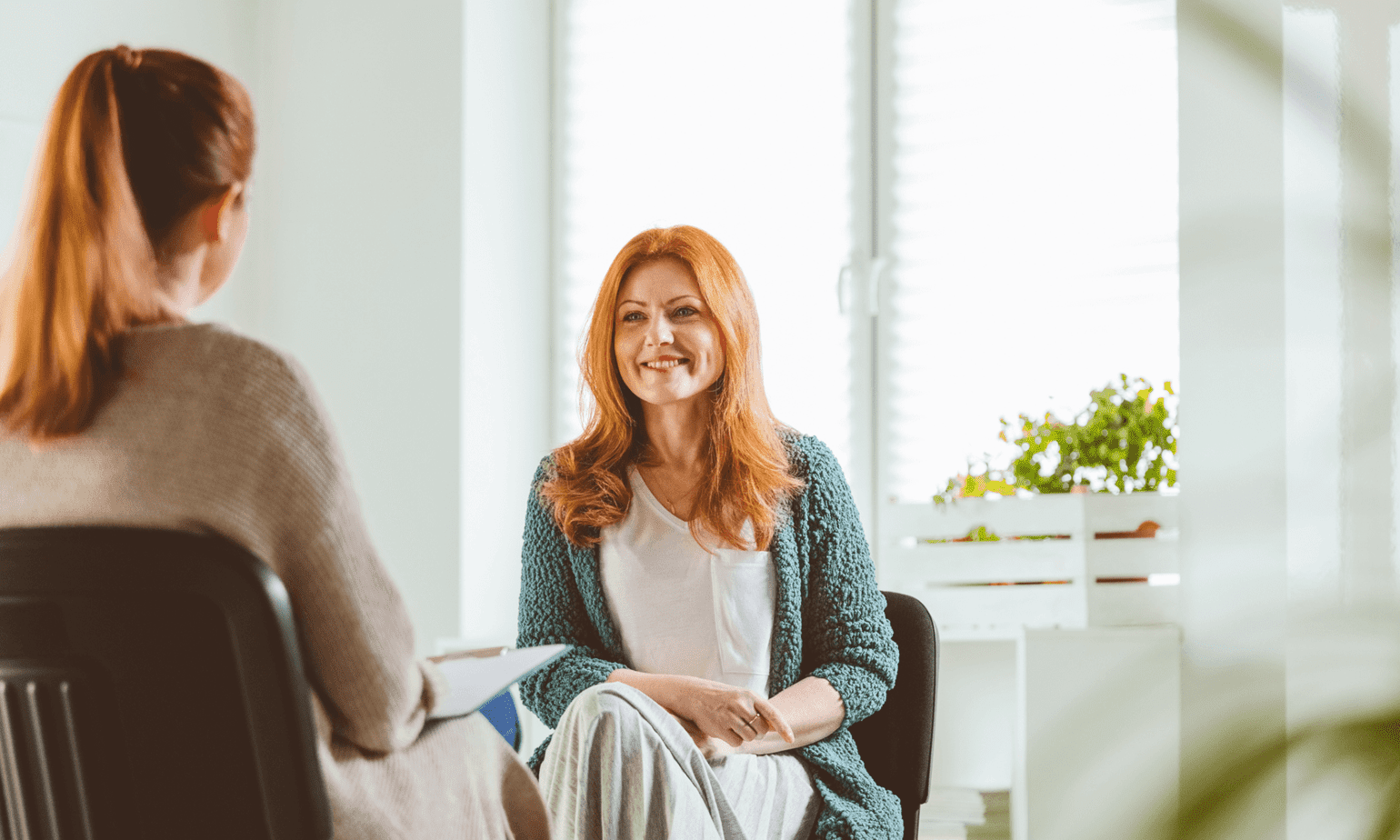 Two women sit on chairs; a female therapist helps a woman in addiction recovery