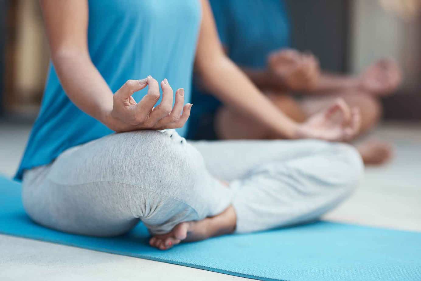 A woman in a blue shirt with gray sweatpants practicing meditation in a drug rehab yoga class.