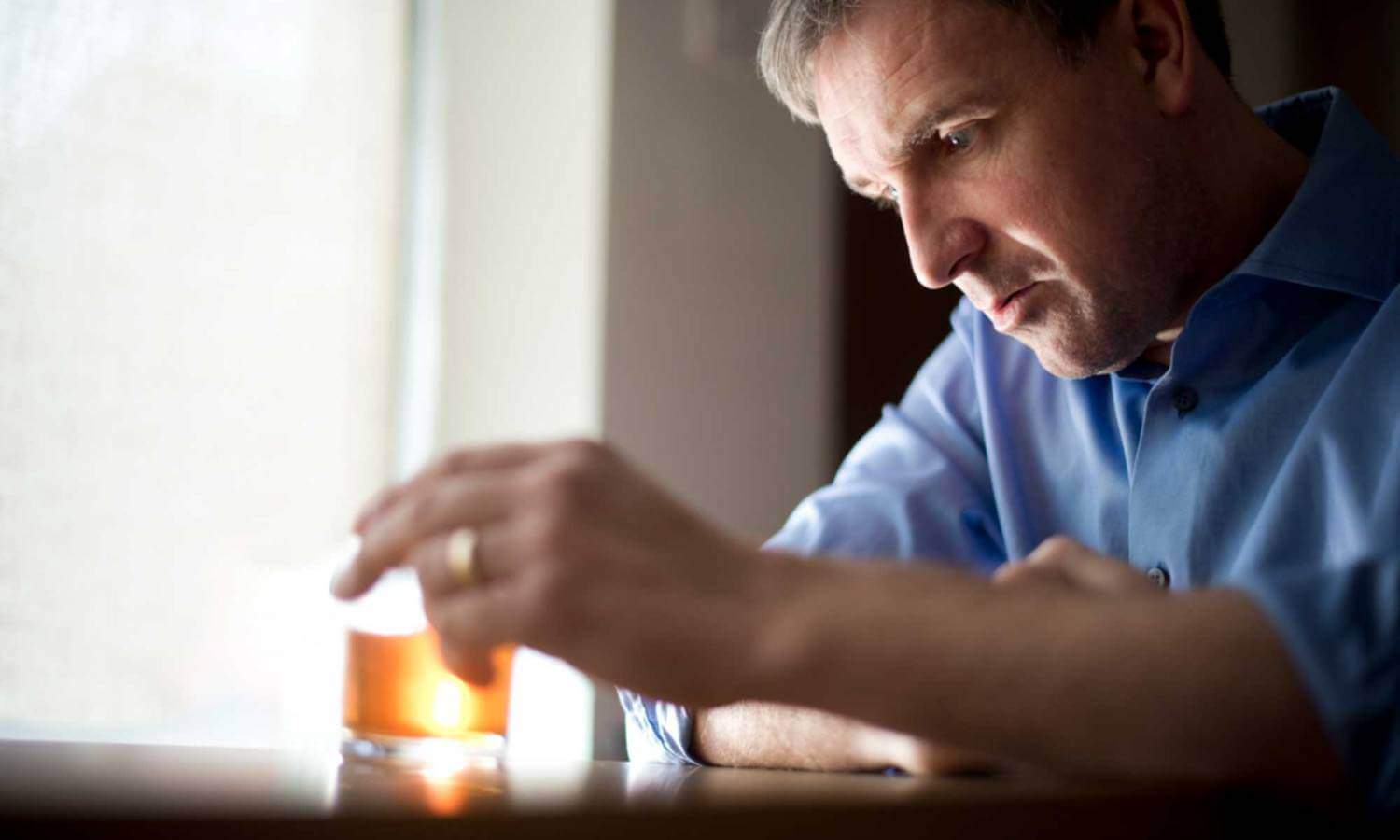 A man sits at a table with a drink and a distressed face.
