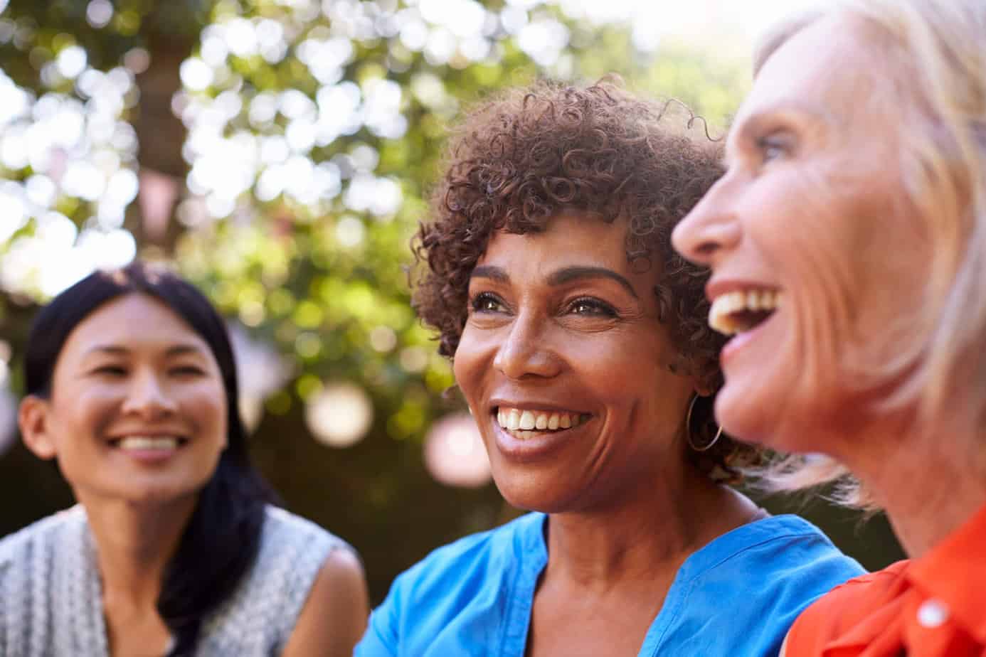 A diverse group of mature women sitting outside and laughing together.