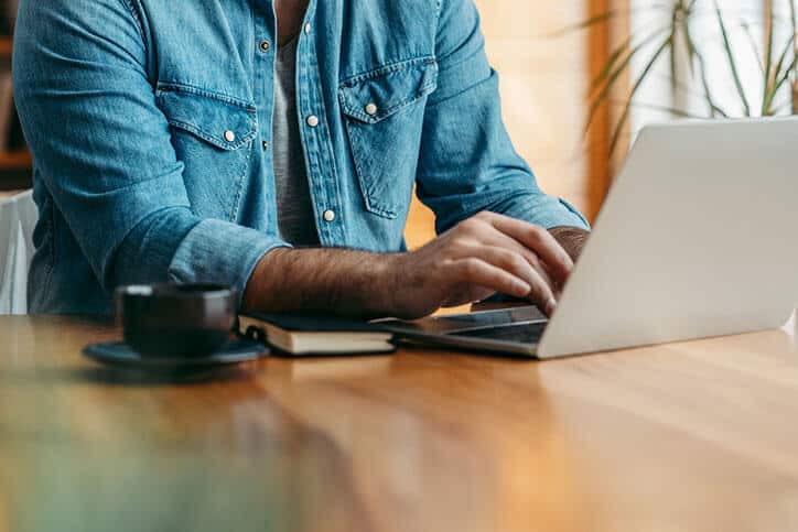 Man in blue denim shirt typing a letter on a laptop in Mountainside Treatment Center