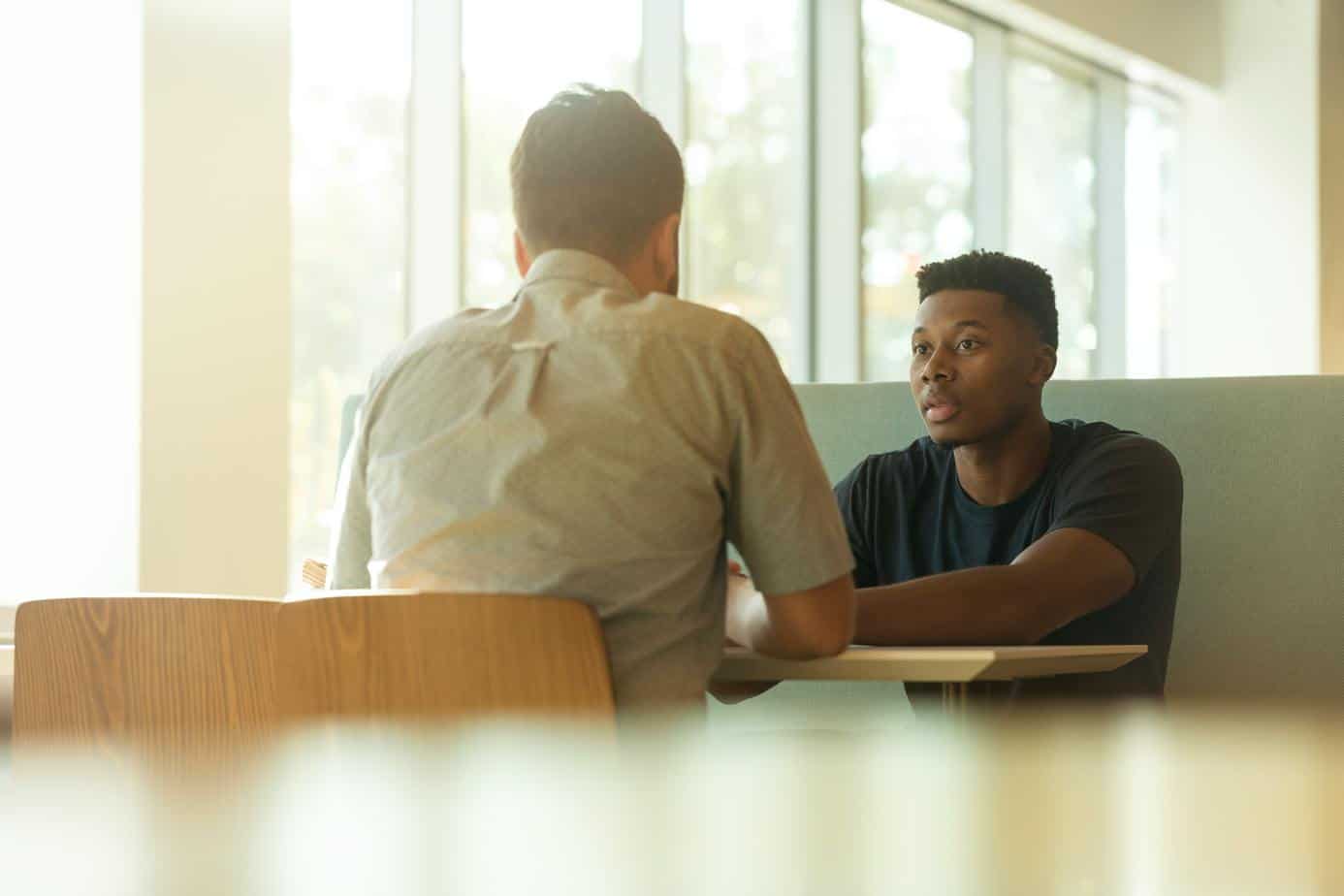 two men have tense conversation in restaurant booth