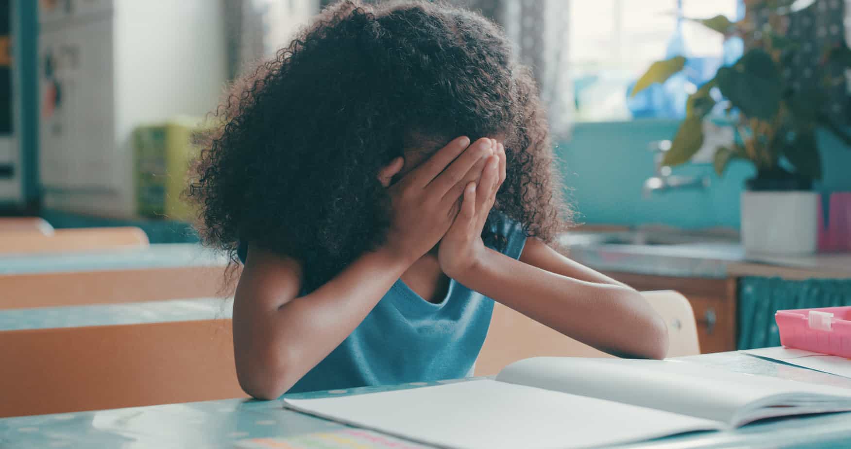 A young black girl covers her face as she does schoolwork at the table
