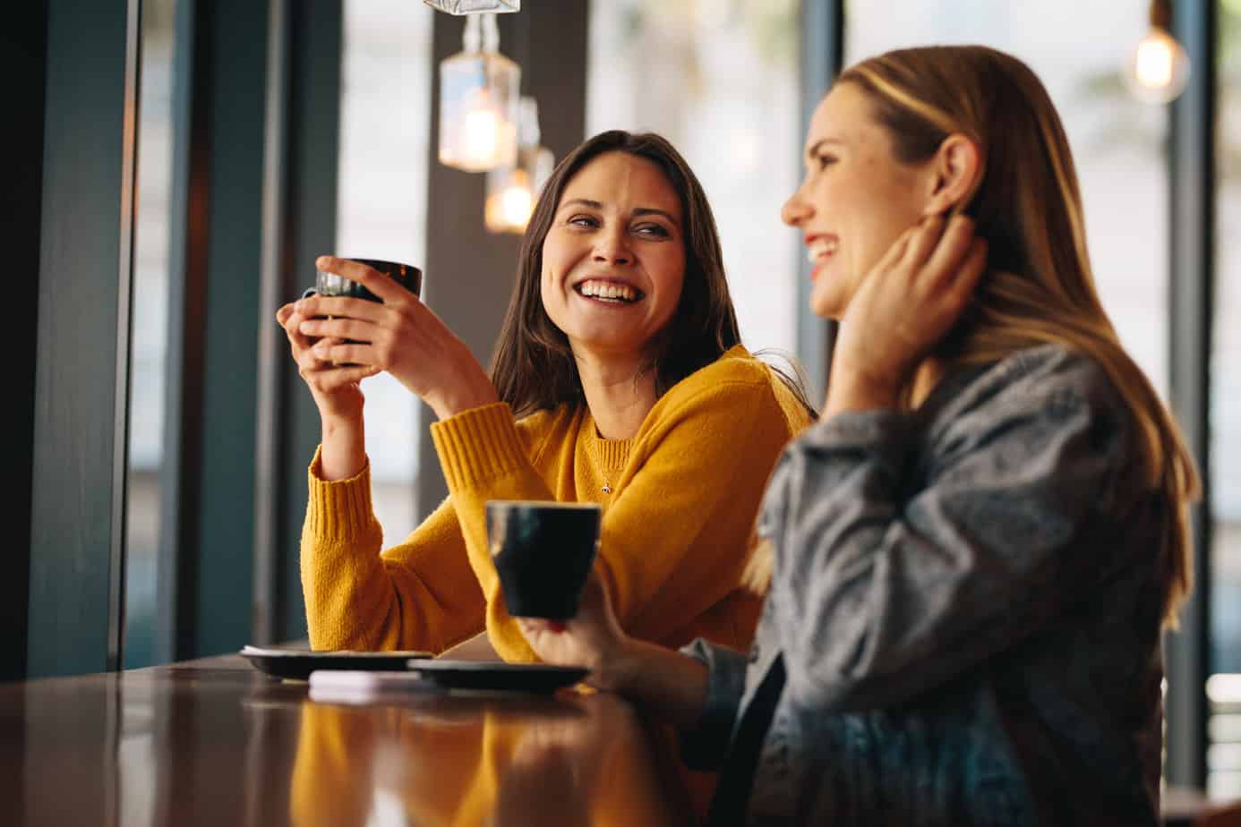 two woman enjoy coffee and conversation seated at high table in restaurant