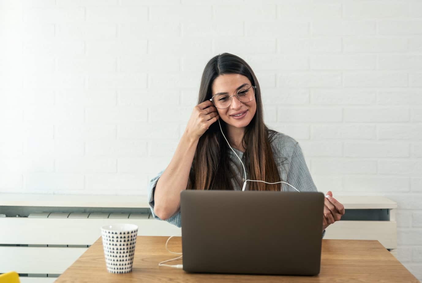 young woman seated in front of computer at table while appreciating benefits of telehealth therapy