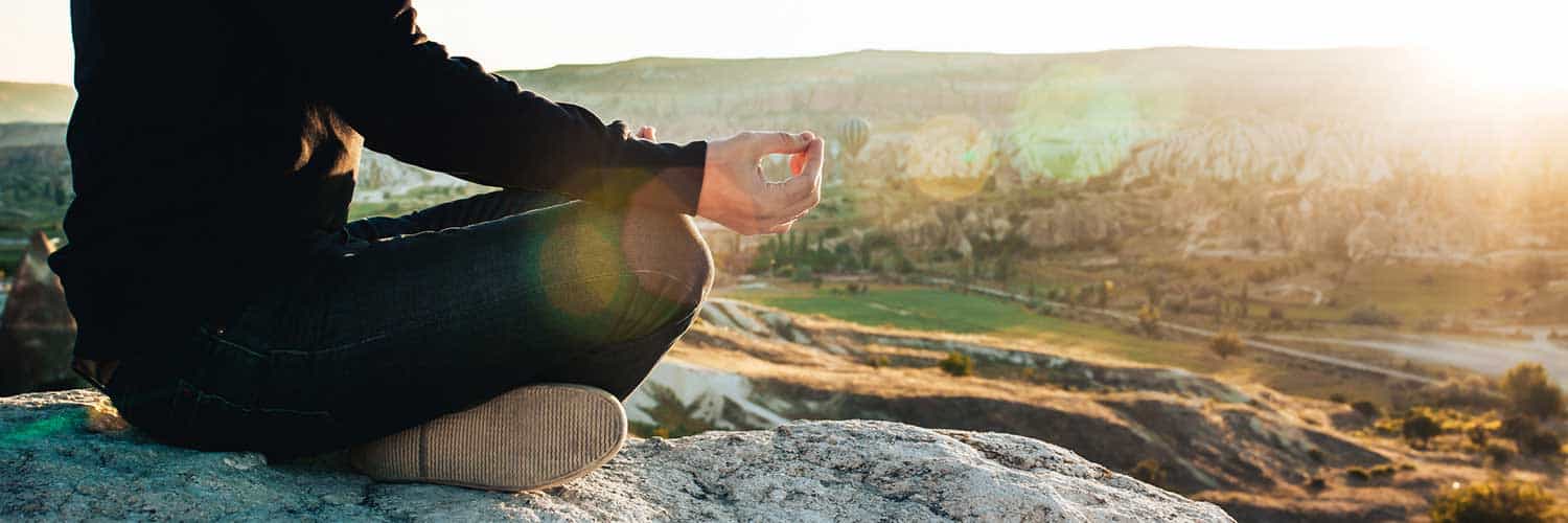 man meditating on a rocky hill in nature