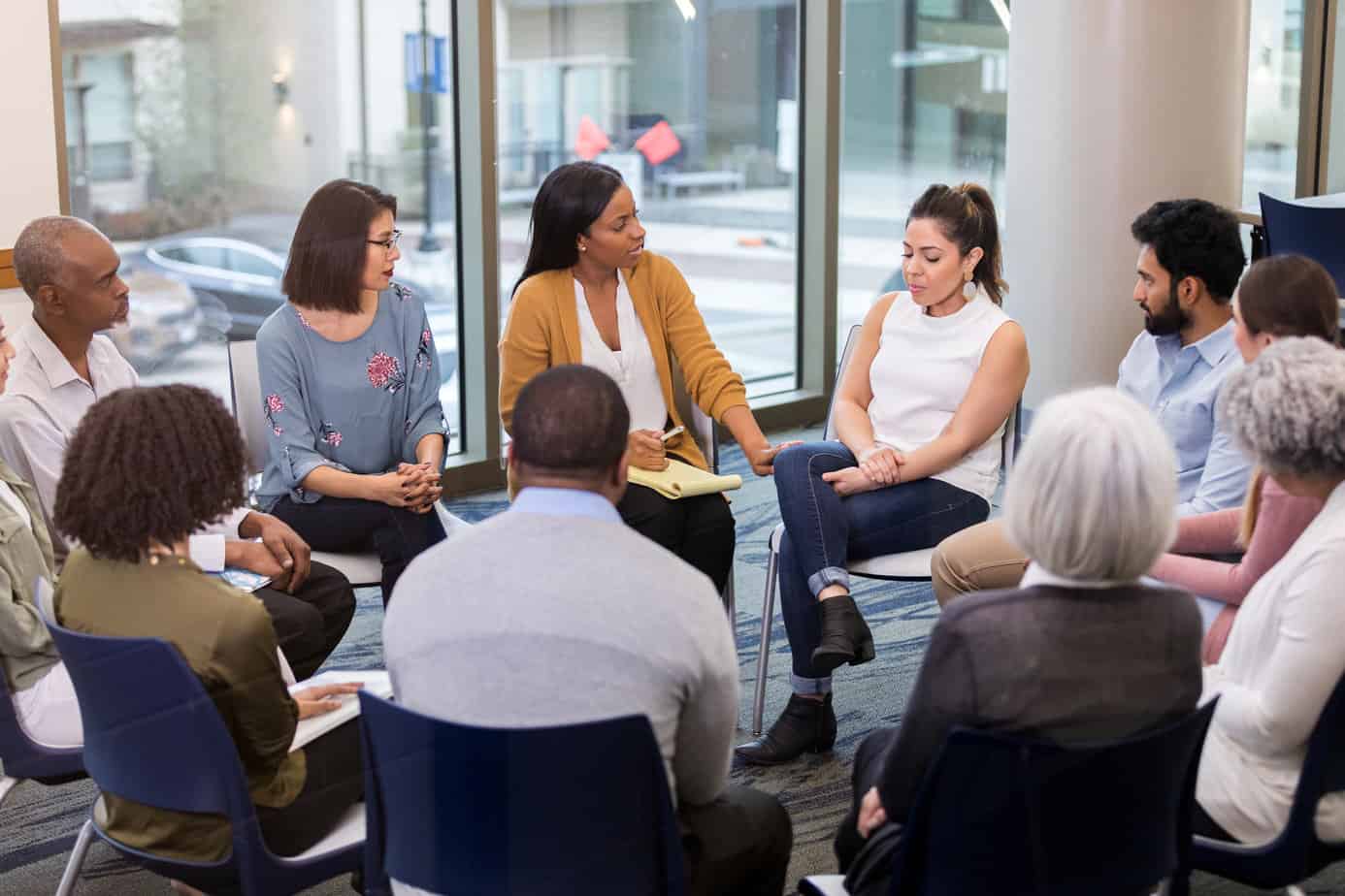 Upset mid adult woman discusses a difficult issue during a support group meeting. A caring mental health professional comforts and speaks encouraging words to the woman.