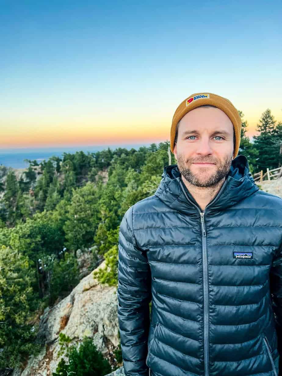man in winter clothing stands on rock in nature at sunrise