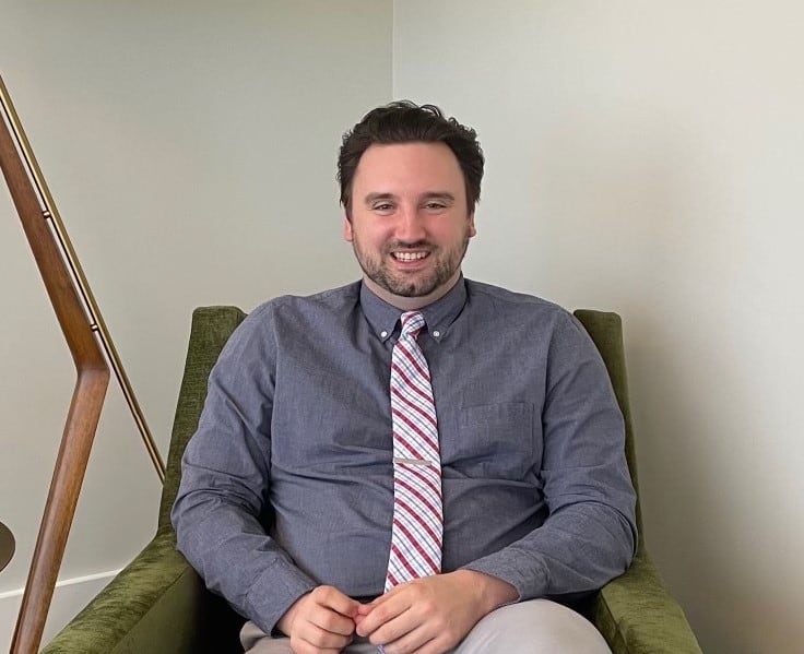 man in formal outfit sitting in living room chair posing for headshot