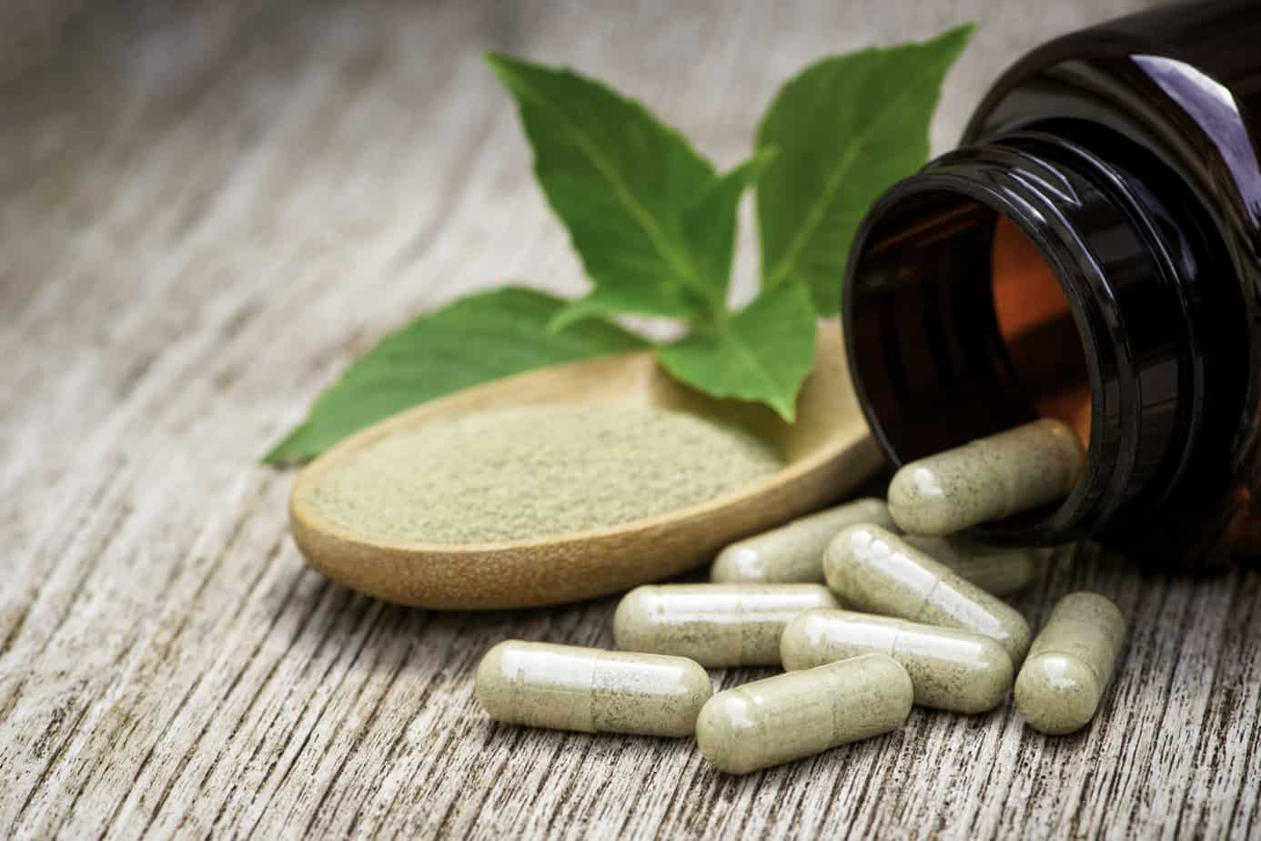 Herbal medicine capsule in brown bottle and herbs powder in wooden spoon with basil leaf on grungy wood table background. Herbs medical plant and nutritional supplement concept.