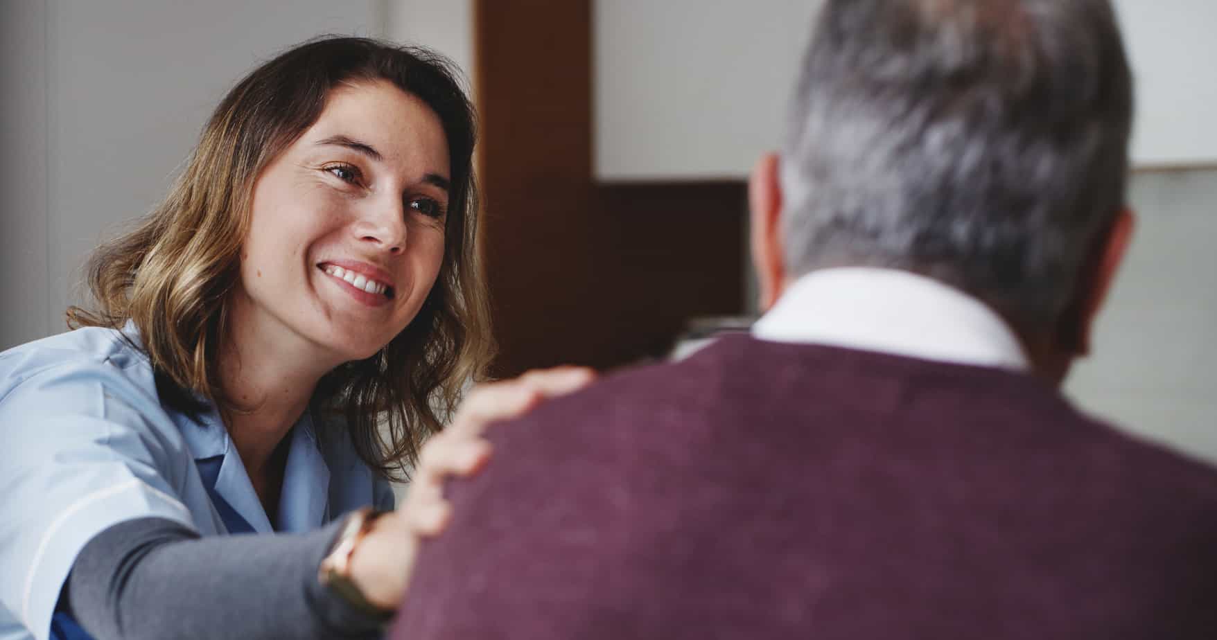 nurse putting a supportive hand on male client's shoulder in rehab