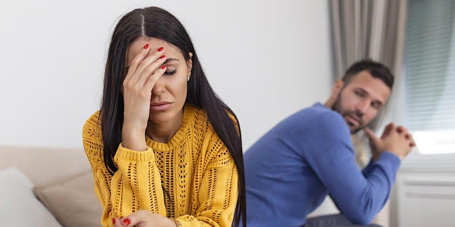 Woman struggling with drug addiction holds her hand to her head with a man upset in the bag round