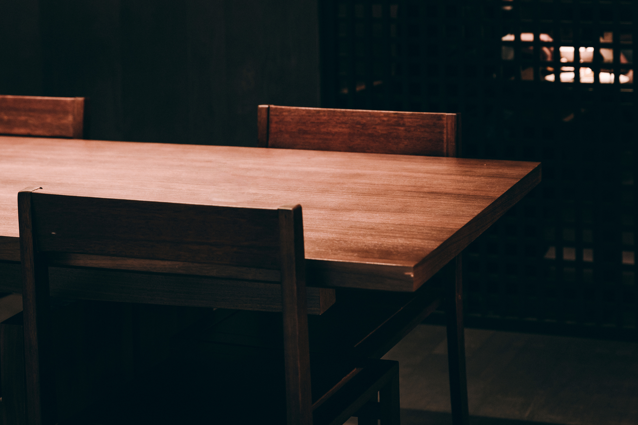 A wooden table in a dark room with two empty chairs opposite each other.