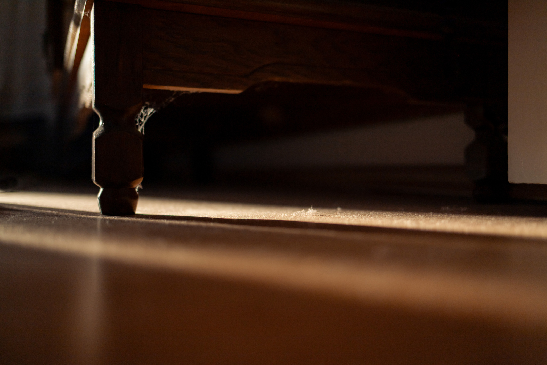 A close-up of a wooden floor and the bottom corner of a bed in soft light.