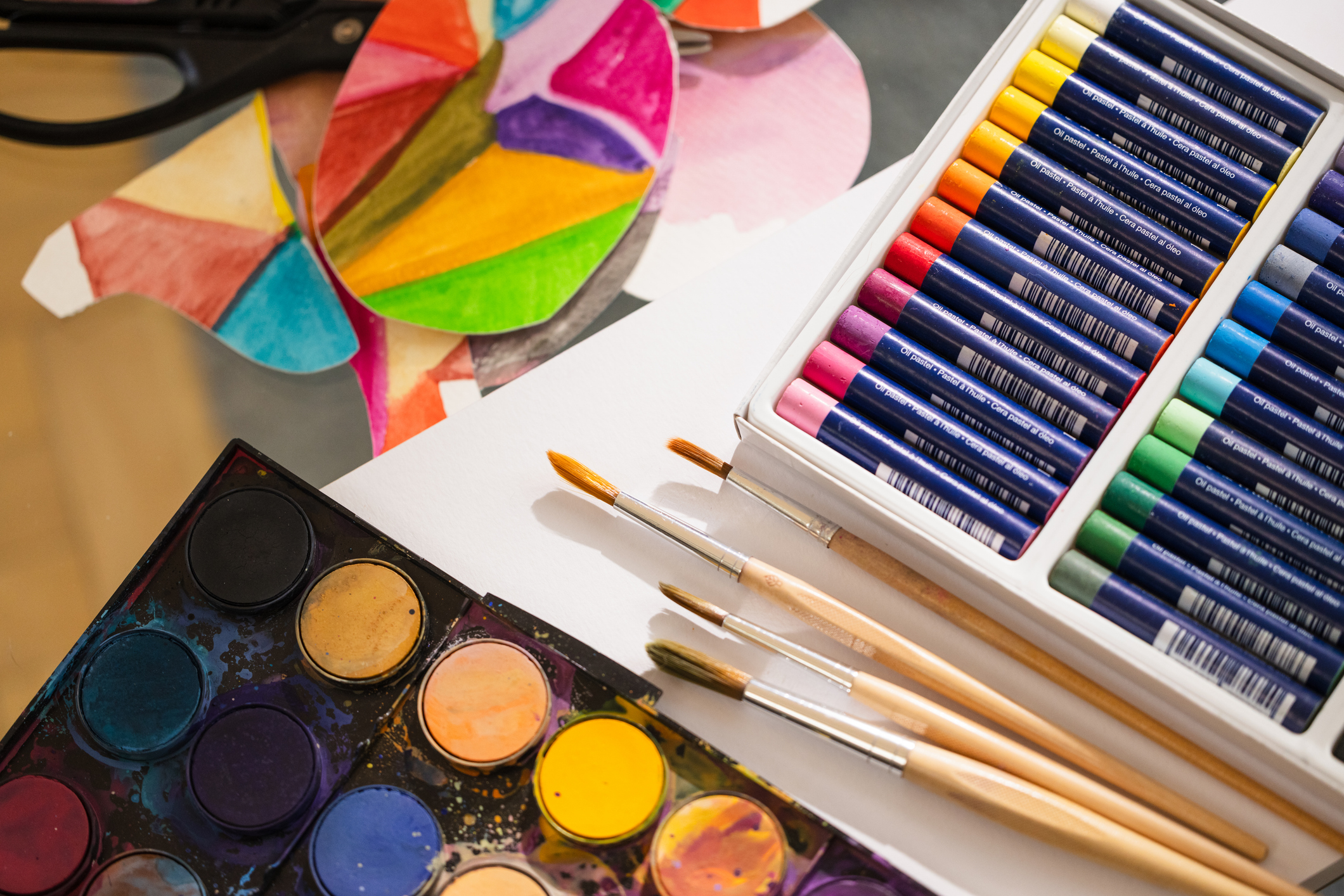An assortment of paintbrushes, pastels, and watercolors lie on a piece of paper and a colored in drawing.