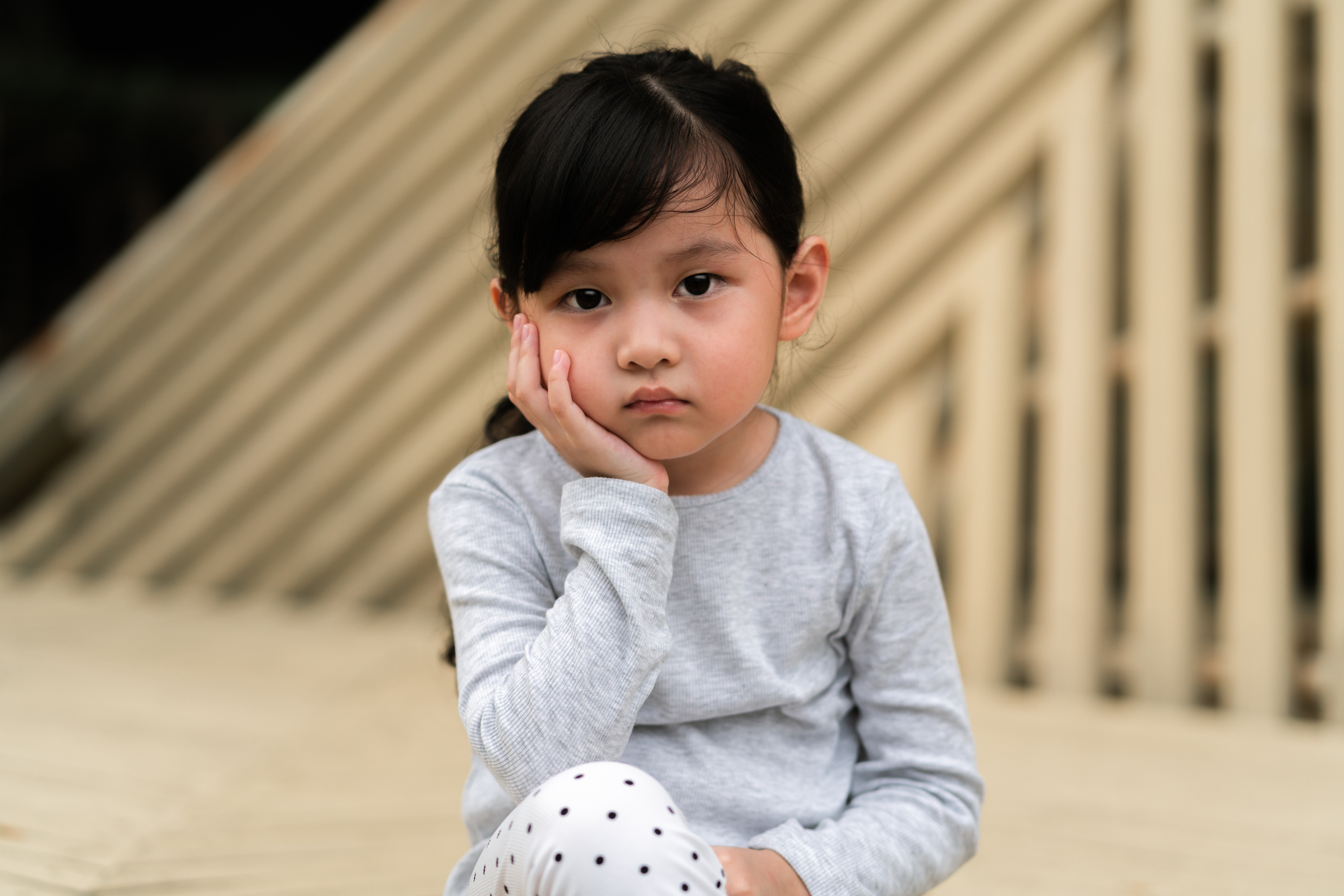 A young girl sits on the floor and rests her head in her hand.