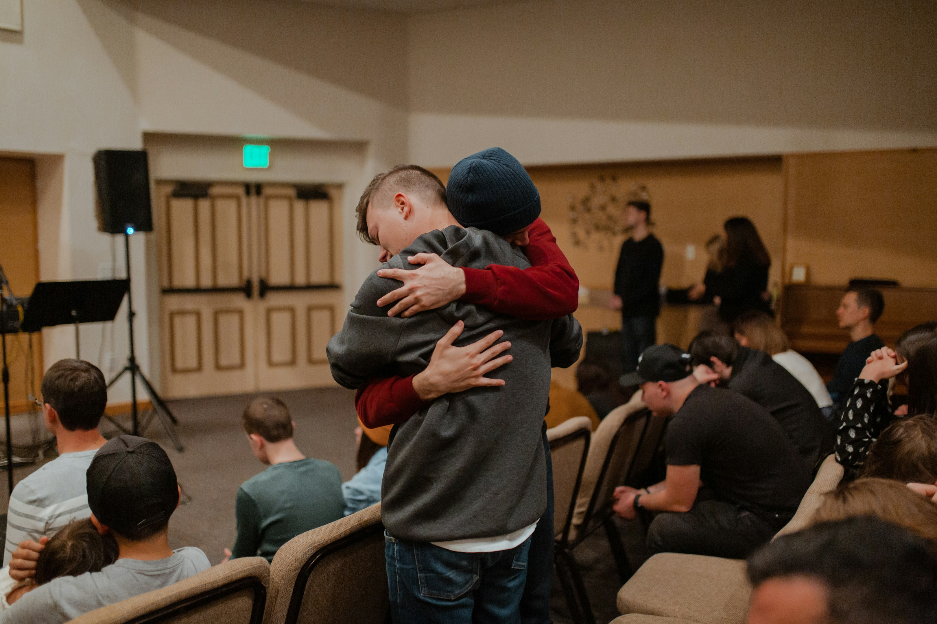Two men using the 12 steps of recovery embrace in a huge during a meeting