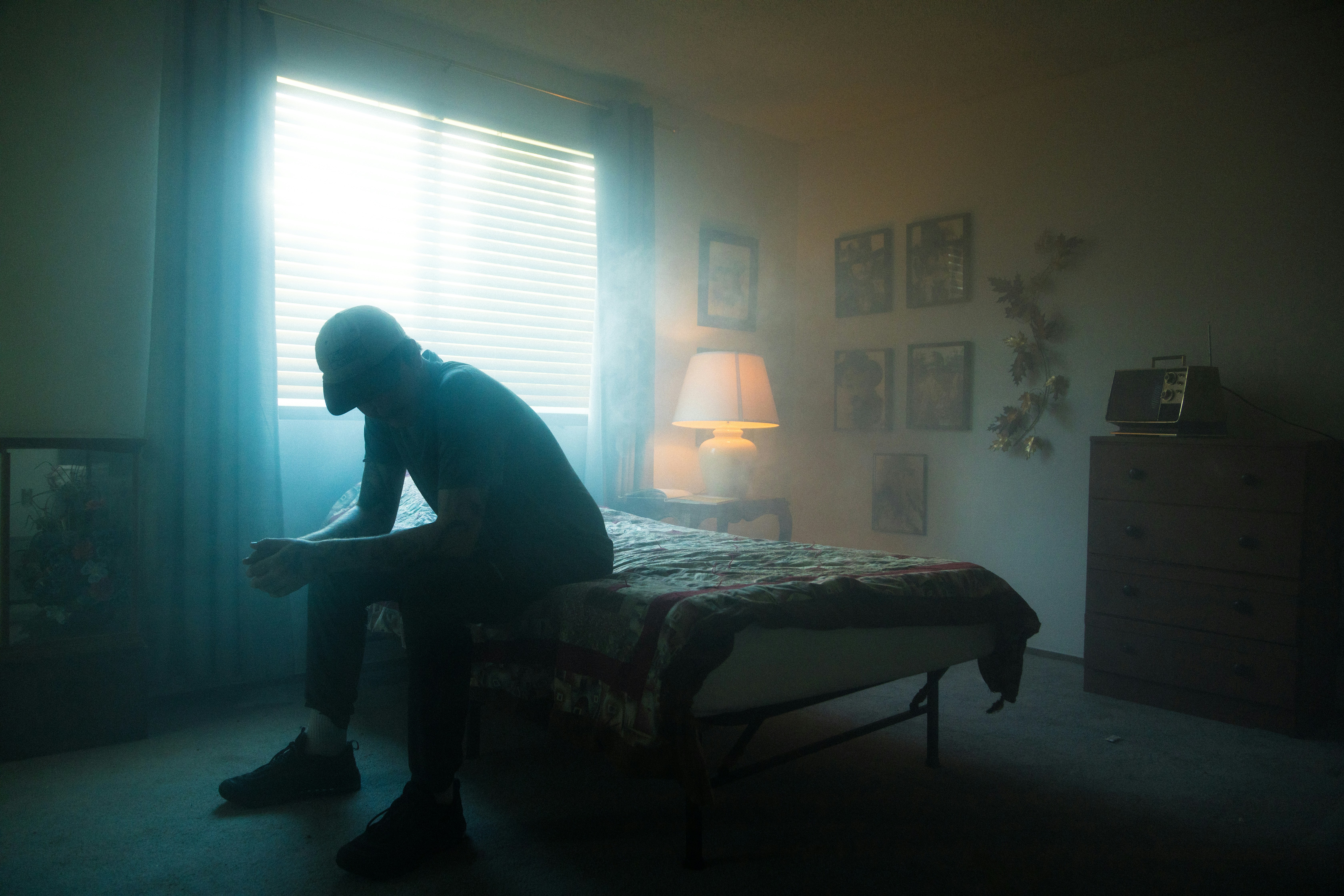 man sits alone on the edge of his bed experiecing the 7 stages of grief