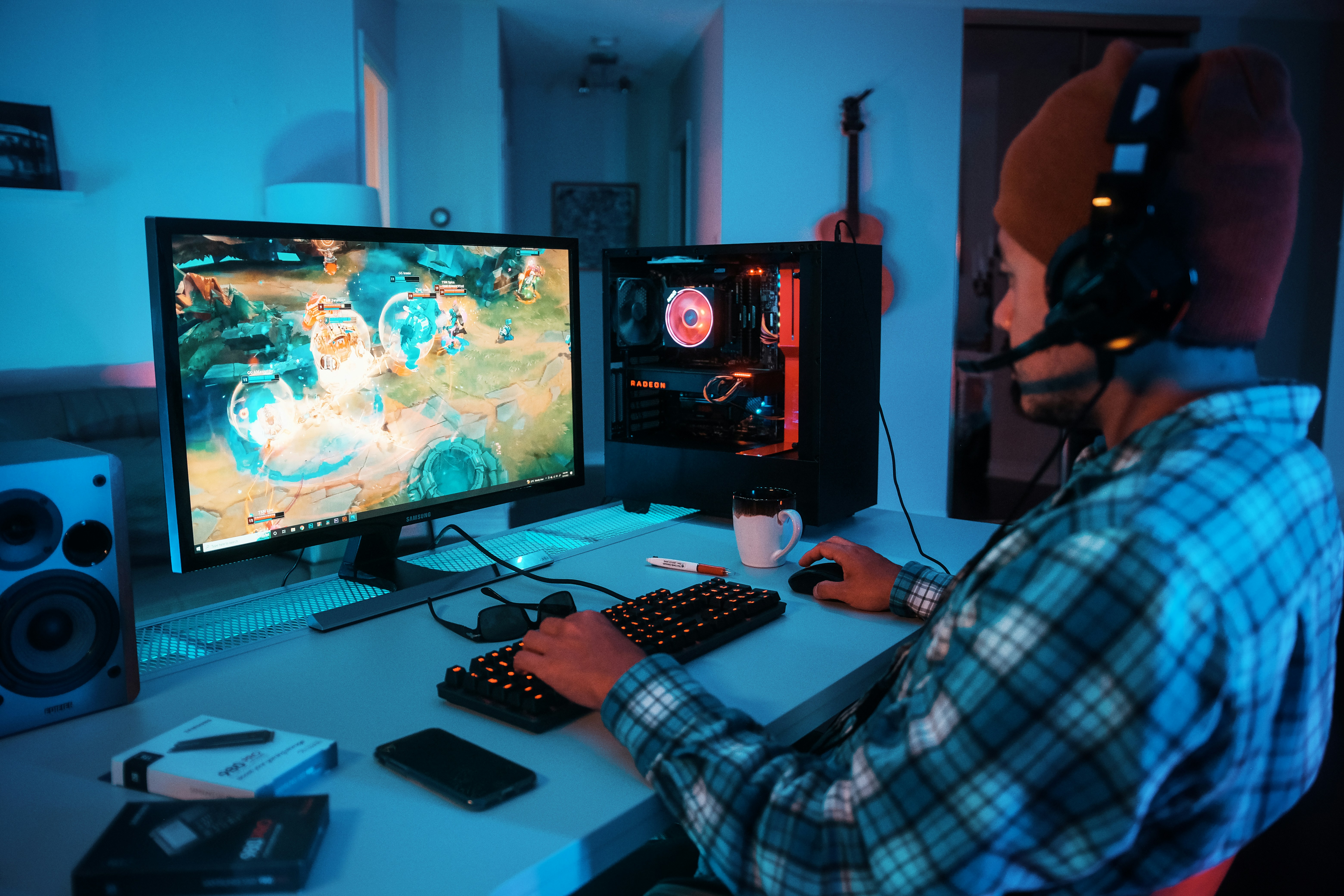 young man with hat and headphones sits at his computer while doing online gaming